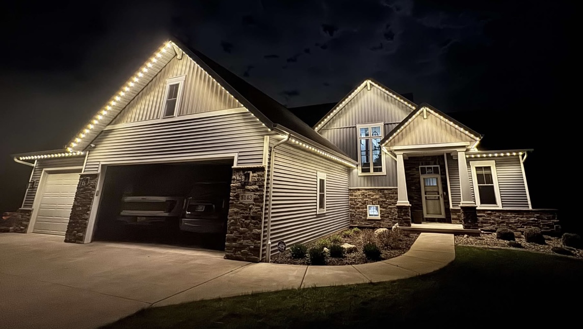 Home with warm white roofline lights glowing against a cloudy night sky