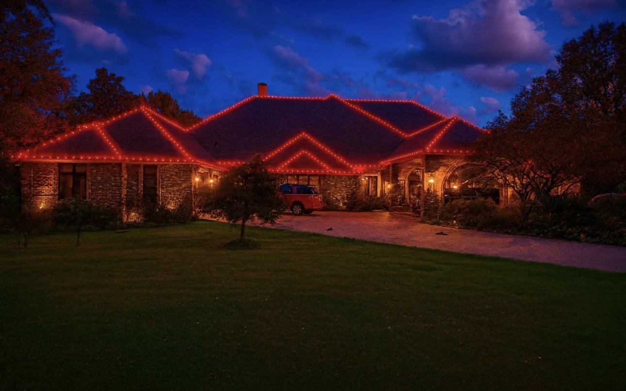 Stone home with red holiday roofline lighting under a deep blue sky