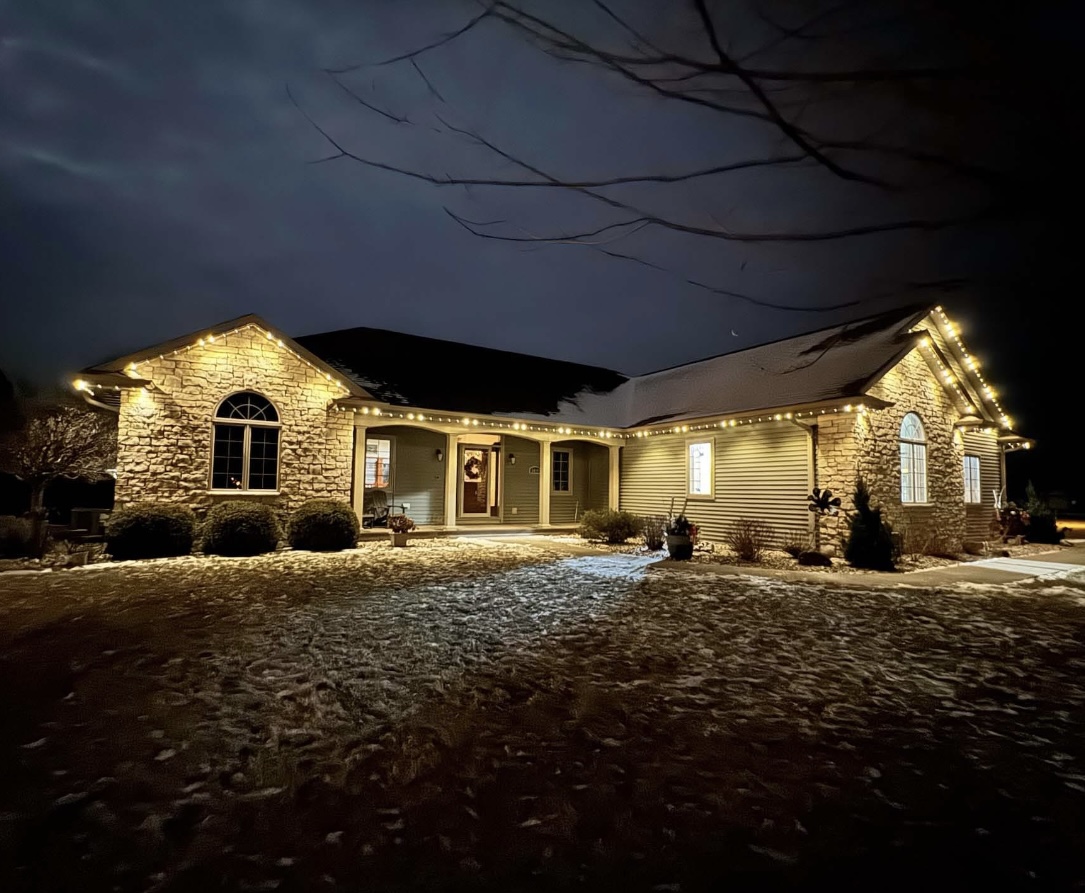 Stone and siding home with warm white holiday lights on a snowy evening