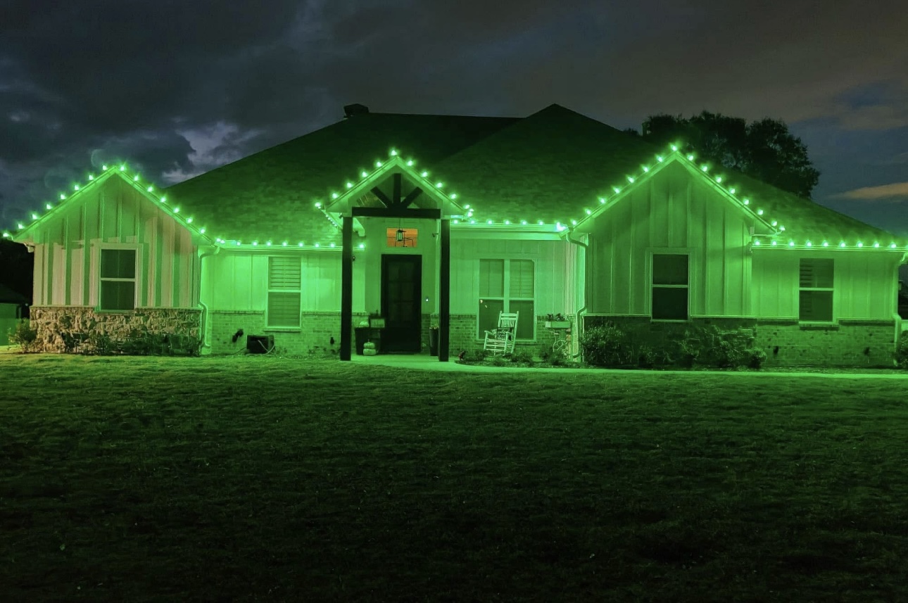 Farmhouse glowing with green holiday roofline lights at night
