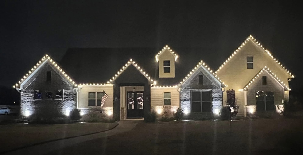 Two-story home with warm white holiday lights tracing every gable