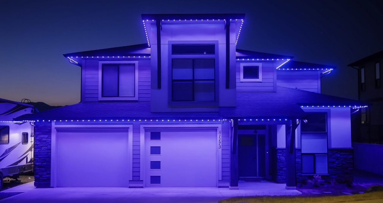 Two-story home washed in purple and blue holiday lighting