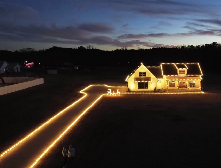 Aerial view of a holiday-lit home with a glowing driveway at dusk